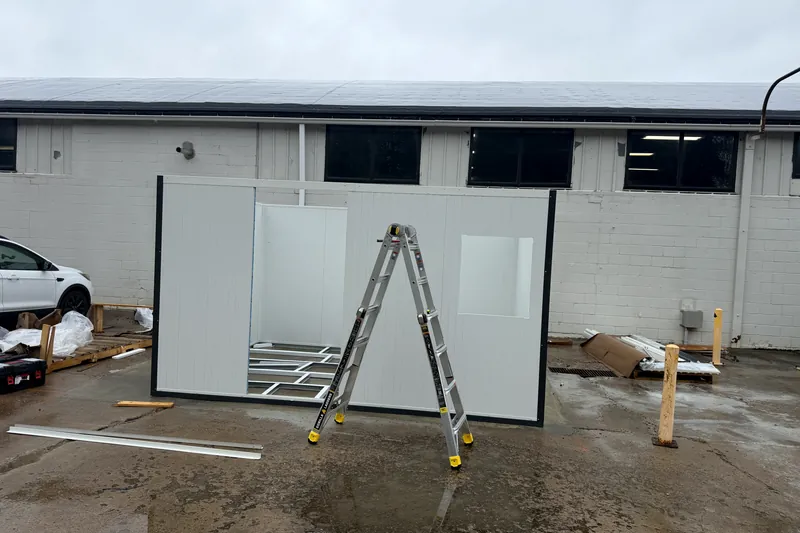 Installer setting insulated wall panels of a modular office, ladder and window opening visible